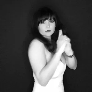 Woman in white sleeveless top posed against dark backdrop, black and white portrait photograph