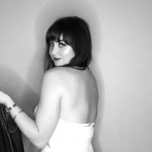Woman in white strapless top with black bob haircut posing over shoulder against neutral backdrop