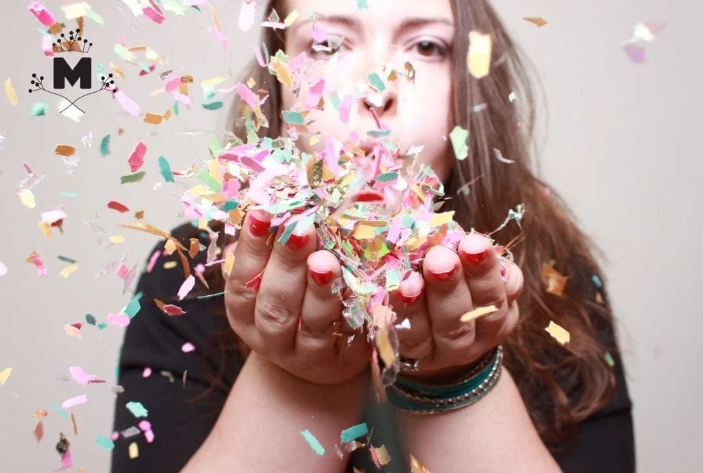 Woman blowing colorful confetti toward camera with playful expression, festive celebration moment
