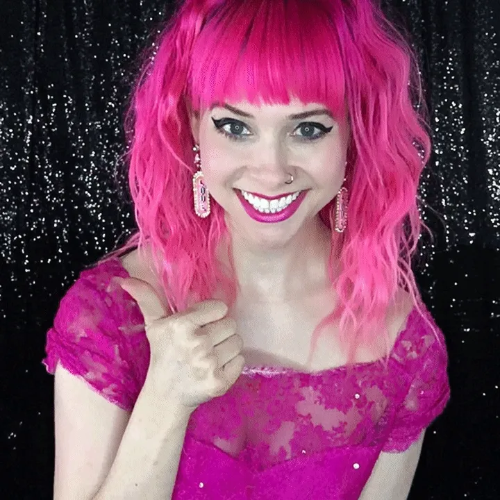 Woman Giving Thumbs-Up in Pink Wig Woman with bright pink wig giving thumbs-up gesture against backdrop