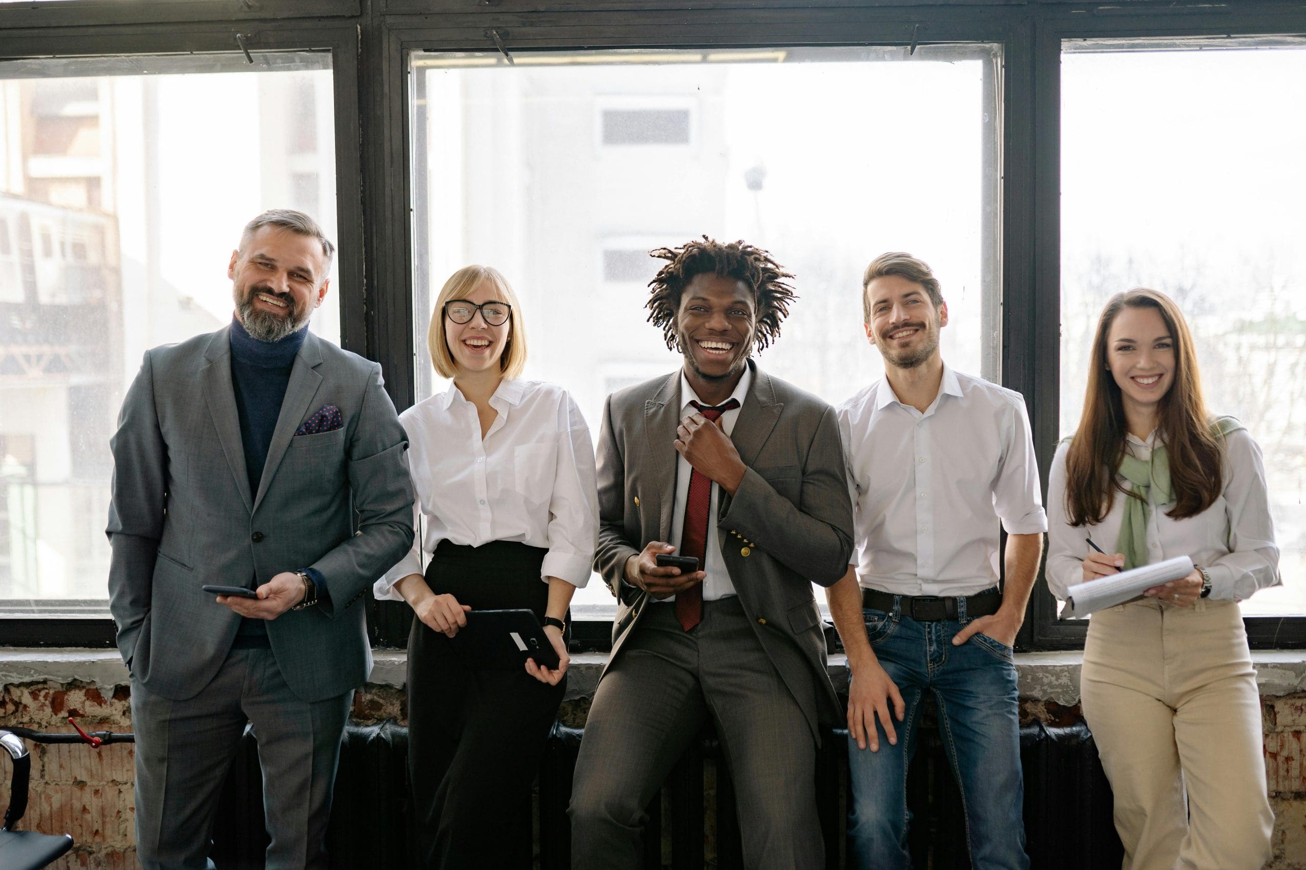 Five diverse team members standing together in casual business attire against a neutral beige background